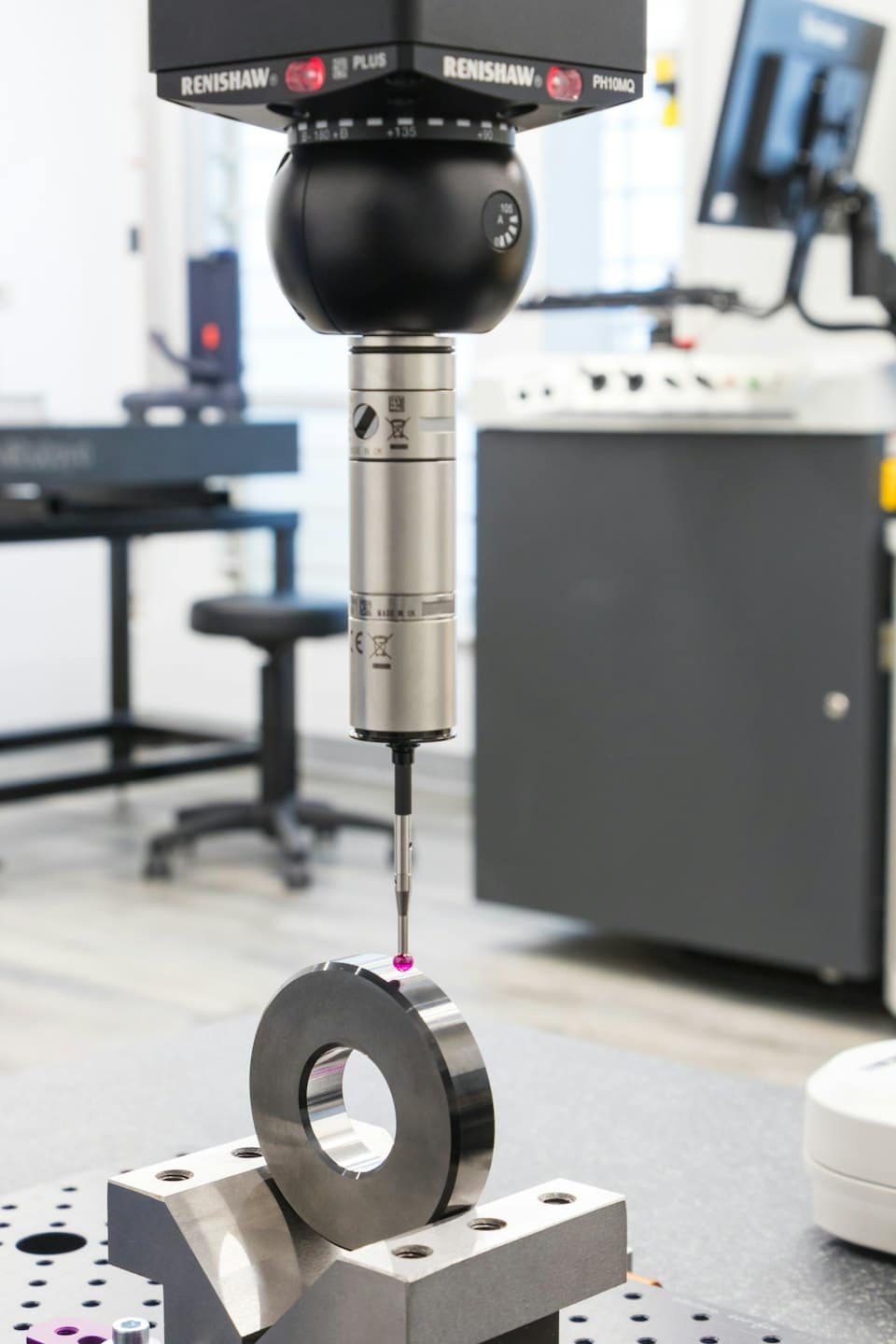 A CMM probe measures a metal component in a lab.